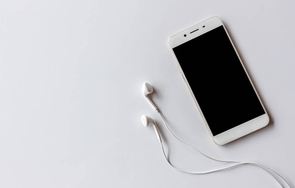 smartphone και ακουστικό σε λευκό τραπέζι με πέρα από το φως στο παρασκήνιο - Φωτογραφία, εικόνα
