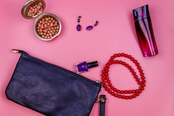 Koppeling zak, rode ketting, oorbellen, nagellak, rouge ballen en fles parfum op roze achtergrond. Schoonheid en mode concept. Vlakke lay, bovenaanzicht - Foto, afbeelding