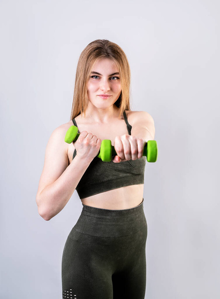 Sports and fitness. Young sportive woman doing exercises with dumbbells isolated on gray - Foto, Bild