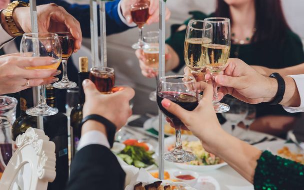 Close up shot of group of people clinking glasses with wine or champagne in front of bokeh background. older people hands. - Foto, Imagen
