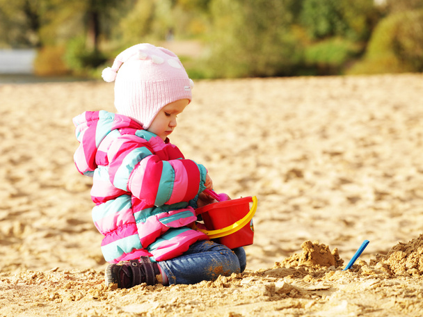 Little girl playing with sand at the autumn beach - Fotografie, Obrázek