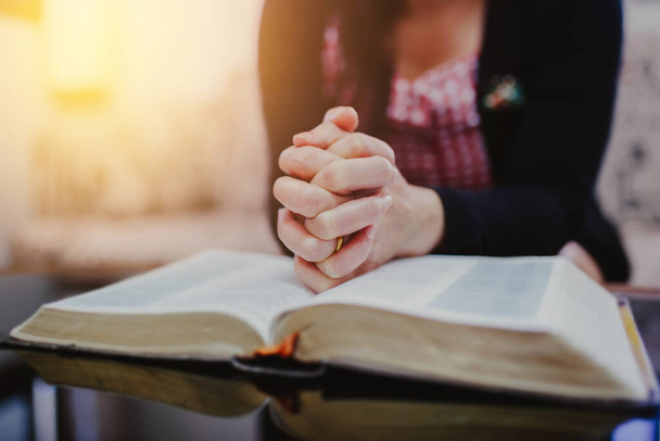 Κοντινό πλάνο των χεριών της γυναίκας προσεύχεται σε ανοιχτή Βίβλο, ενώ κάθεται στον καναπέ στο σπίτι - Φωτογραφία, εικόνα