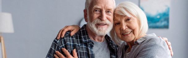 imagen horizontal de feliz pareja de ancianos sonriendo y abrazando mientras mira a la cámara
 - Foto, imagen