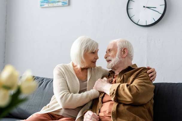 selective focus of happy senior couple sitting on sofa and looking at each other - Fotoğraf, Görsel