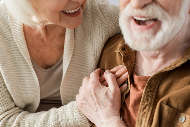 ostříhaný pohled na rozesmátý starší pár držící se za ruce, selektivní zaměření - Fotografie, Obrázek