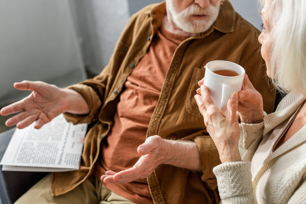 cropped view of senior man showing shrug gesture while talking to woman holding cup of tea - Foto, Bild