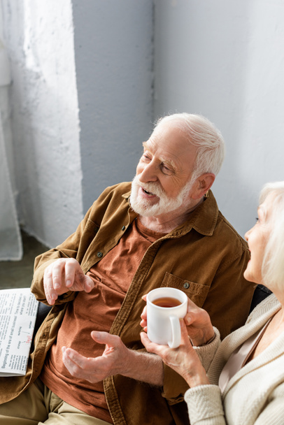 високий кут зору усміхнений старший чоловік розмовляє з дружиною тримає чашку чаю
 - Фото, зображення