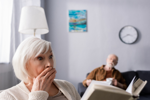 selective focus of senior man looking at shocked wife reading book  - Photo, Image