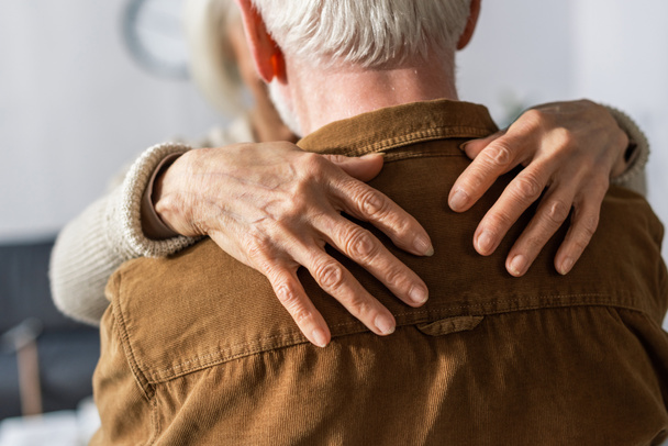 Rückansicht eines älteren Mannes, der von seiner Frau umarmt wird - Foto, Bild