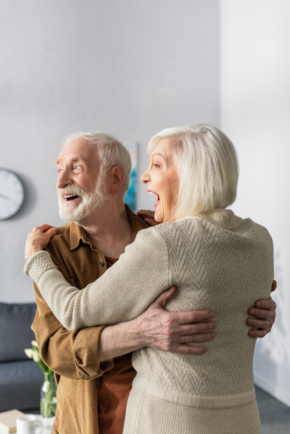 happy senior couple dancing, laughing and looking away at home - Foto, imagen