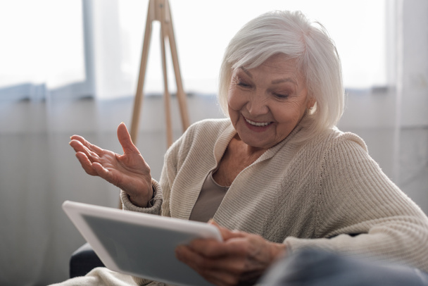 enfoque selectivo de la mujer mayor alegre sentado con el brazo abierto mientras se utiliza la tableta digital
 - Foto, Imagen