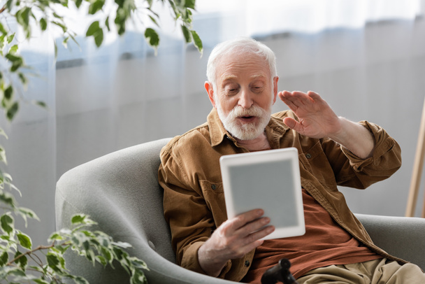 Dijital tablet üzerindeki video çağrısı sırasında el sallayan mutlu yaşlı adamın seçici odağı - Fotoğraf, Görsel