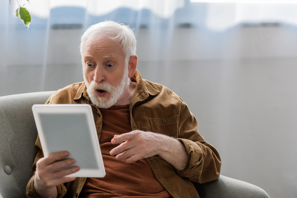 sorprendido hombre mayor señalando con el dedo mientras se utiliza la tableta digital
 - Foto, imagen