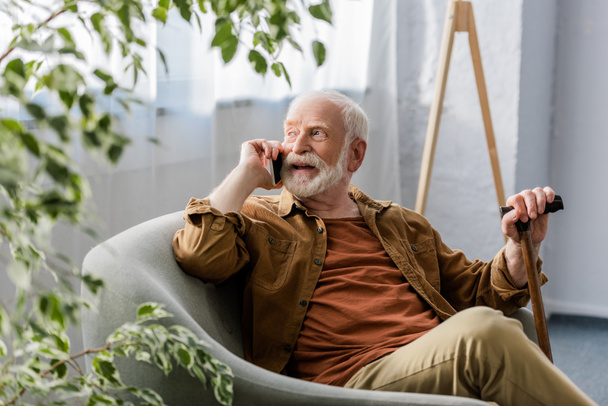 selektywne skupienie szczęśliwego seniora siedzącego w fotelu i mówiącego na smartfonie - Zdjęcie, obraz