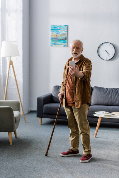 счастливый пожилой человек стоит с тростью и делает селфи на смартфоне
 - Фото, изображение