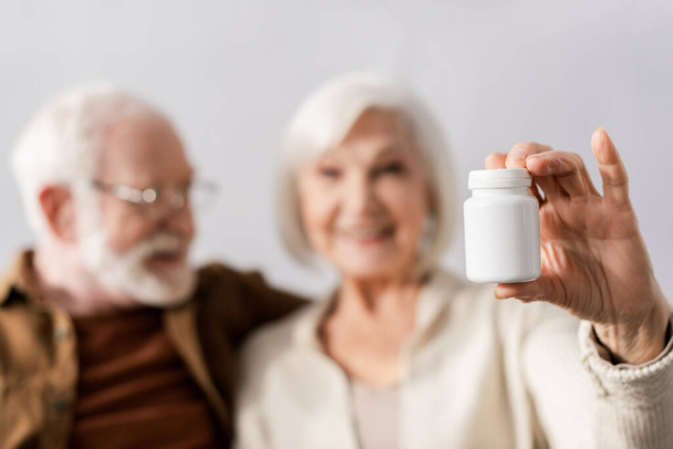 selective focus of smiling senior woman showing pills container near cheerful man - Foto, imagen