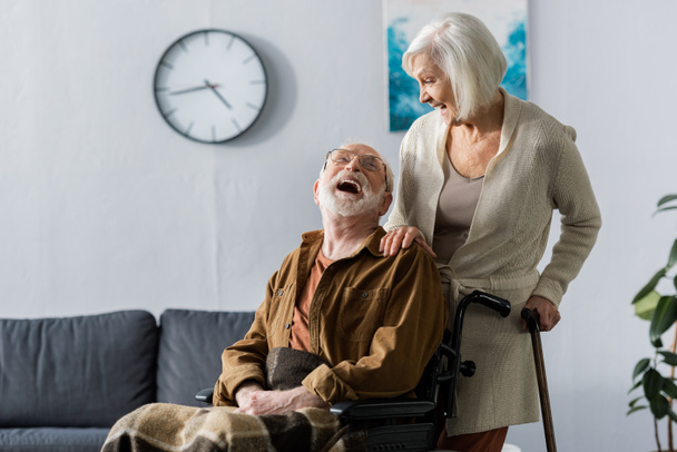 esposa mayor y marido alegre en silla de ruedas riendo mientras se miran
 - Foto, Imagen