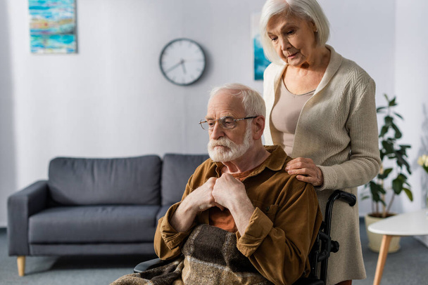 smutna, starsza kobieta dotykająca ramienia niepełnosprawnego męża, chora na demencję - Zdjęcie, obraz