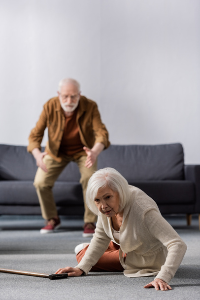 selektywna ostrość seniora spiesząc się pomóc żonie leżącej na podłodze w pobliżu kija - Zdjęcie, obraz
