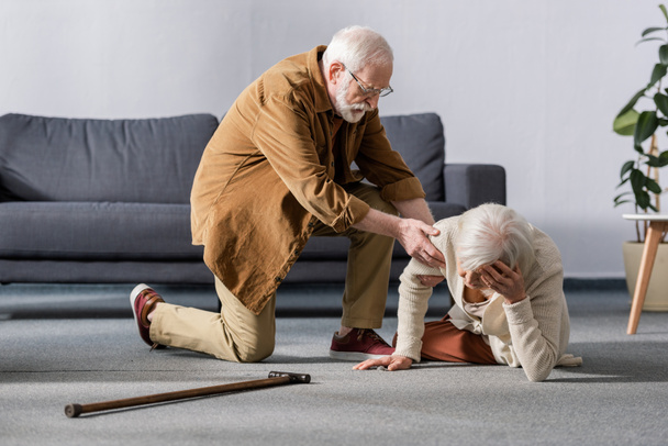 hombre mayor ayudando a la esposa acostada en el suelo y tocando la cabeza
 - Foto, Imagen