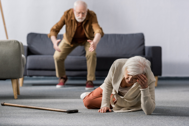 enfoque selectivo del hombre mayor que se apresura a ayudar a la esposa acostada en el suelo cerca de bastón
 - Foto, Imagen