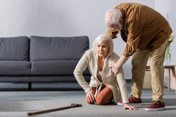 senior hombre ayudando esposa sentado en piso cerca de caminar palo
 - Foto, Imagen