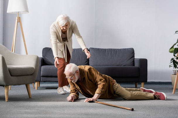 idősebb nő segít felkelni elesett férj feküdt a padlón mellett sétapálca - Fotó, kép