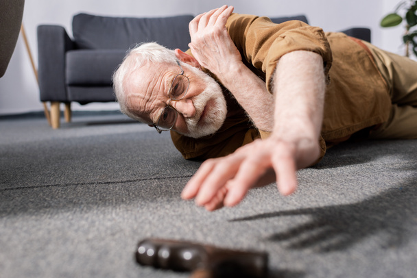 szelektív fókusz tehetetlen idős férfi elesett a padlón, és próbál kap sétapálca - Fotó, kép