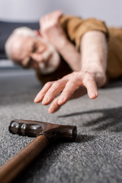 szelektív fókusz tehetetlen idős férfi feküdt a padlón, és próbál kap sétapálca - Fotó, kép