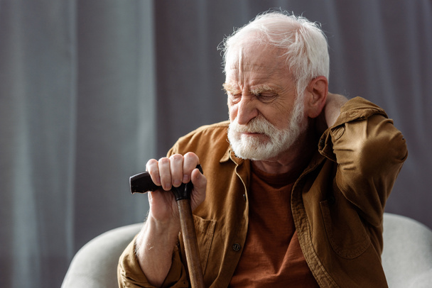 anciano solitario sentado con los ojos cerrados, tocando el cuello y sosteniendo el bastón
  - Foto, imagen
