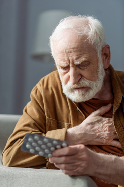 homme âgé solitaire toucher la poitrine tout en se sentant mal et tenant des pilules - Photo, image