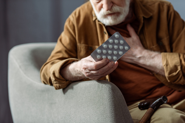 selective focus of senior man touching chest and holding pills while feeling bad - Photo, Image