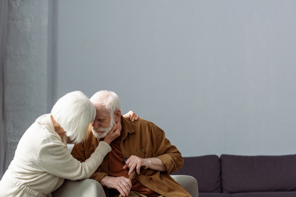 ηλικιωμένη γυναίκα που αγγίζει το πρόσωπο και αγκαλιάζει τον σύζυγο άρρωστο από άνοια - Φωτογραφία, εικόνα