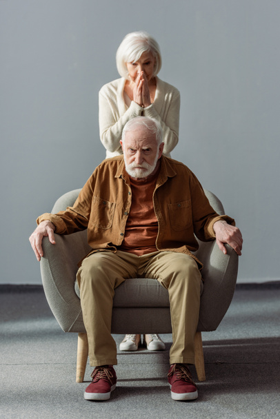 шокована старша жінка торкається обличчя, стоячи за чоловіком, хвора на деменцію
 - Фото, зображення