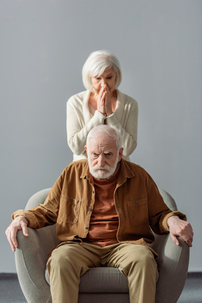 mujer mayor desesperada tocando la cara mientras está de pie detrás del marido, enfermo de demencia
 - Foto, imagen