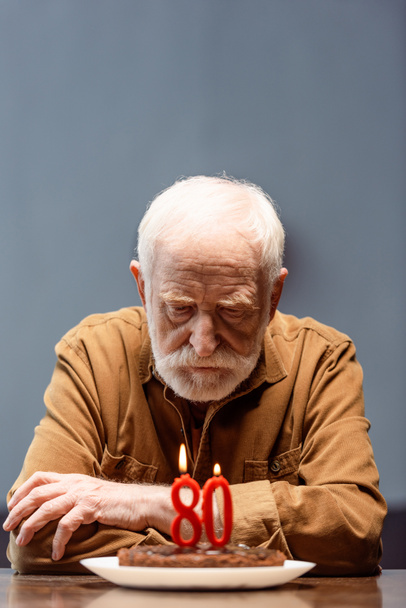 starszy samotny mężczyzna siedzi z skrzyżowanymi ramionami przy torcie urodzinowym z numerem osiemdziesiąt - Zdjęcie, obraz