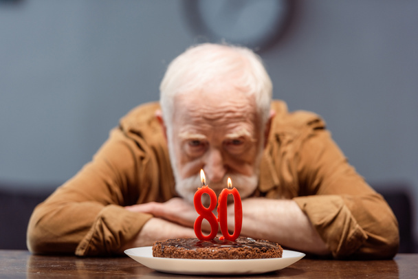 selective focus of lonely senior man looking at birthday cake with number eighty - Photo, Image