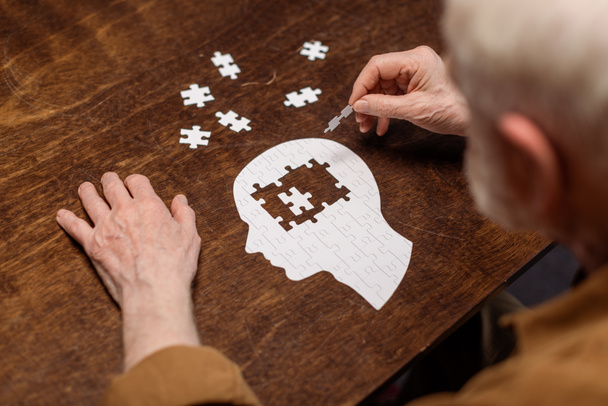 hoge hoek uitzicht van senior man het verzamelen van legpuzzel als dementie rehab - Foto, afbeelding