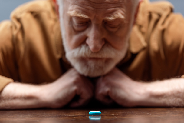 selective focus of old man looking at pill on table - Photo, Image