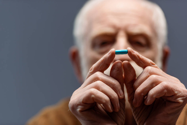 selectieve focus van senior man kijken naar pil in zijn handen - Foto, afbeelding