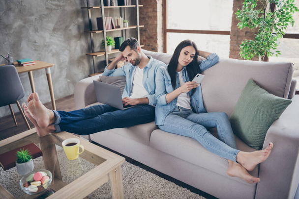 Full size photo of lazy tired two people man freelancer work remote laptop tired read project woman use smartphone chatting texting typing sit comfort cozy couch in house indoors - Foto, imagen
