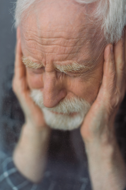 foyer sélectif de l'homme âgé, déprimé avec les yeux fermés touchant le visage près du verre de fenêtre - Photo, image