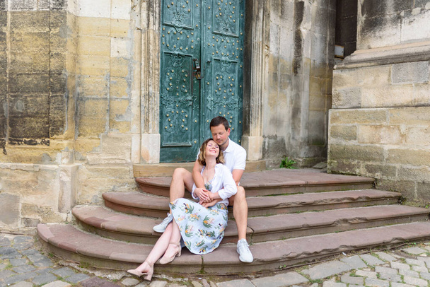 Dois amantes estão sentados nos degraus de uma igreja antiga. O tipo abraça a rapariga por trás. O casal está feliz.
. - Foto, Imagem