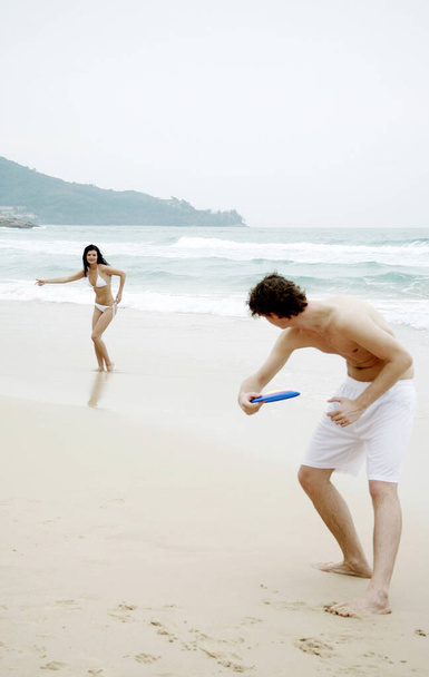 Пара, играющая во фрисби на пляже - Фото, изображение