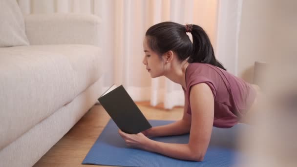 Aziatisch jong vrouw planking en lezen op hetzelfde moment, oefening tijdens covid-19 lock down, thuis uit te oefenen in de woonkamer met sofa, home onderwijs college student beoordeling studie nota lezing - Video