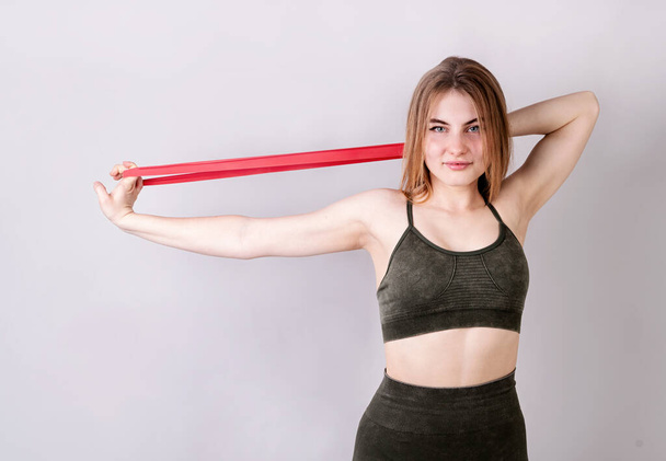 Fitness and sport. Young fit woman doing exercises with a resistance band isolated on gray - Photo, Image