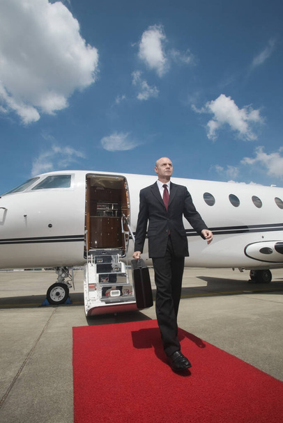 Businessman walking on red carpet upon exiting private jet - Foto, afbeelding