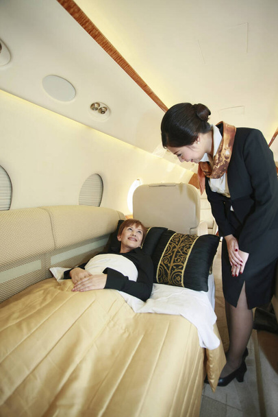 Flight attendant checking on resting businesswoman - Foto, imagen