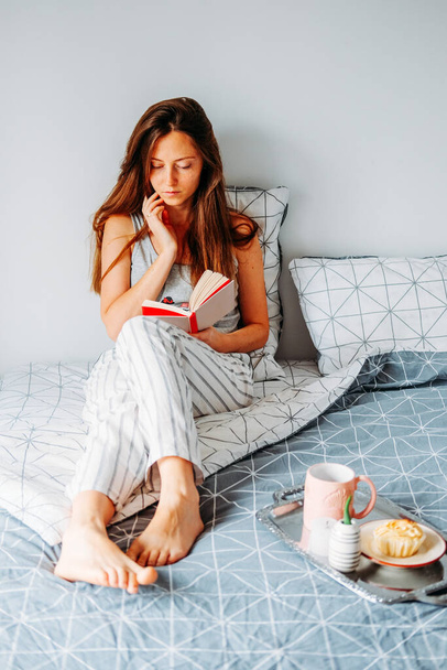 Jonge roodharige vrouw die in bed leest. Luie ochtend routine. - Foto, afbeelding