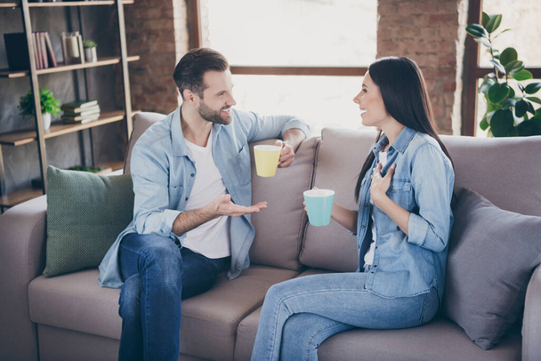 Photo of positive caring married people man woman sit couch hold mug beverage have talk news in house indoors - Photo, Image